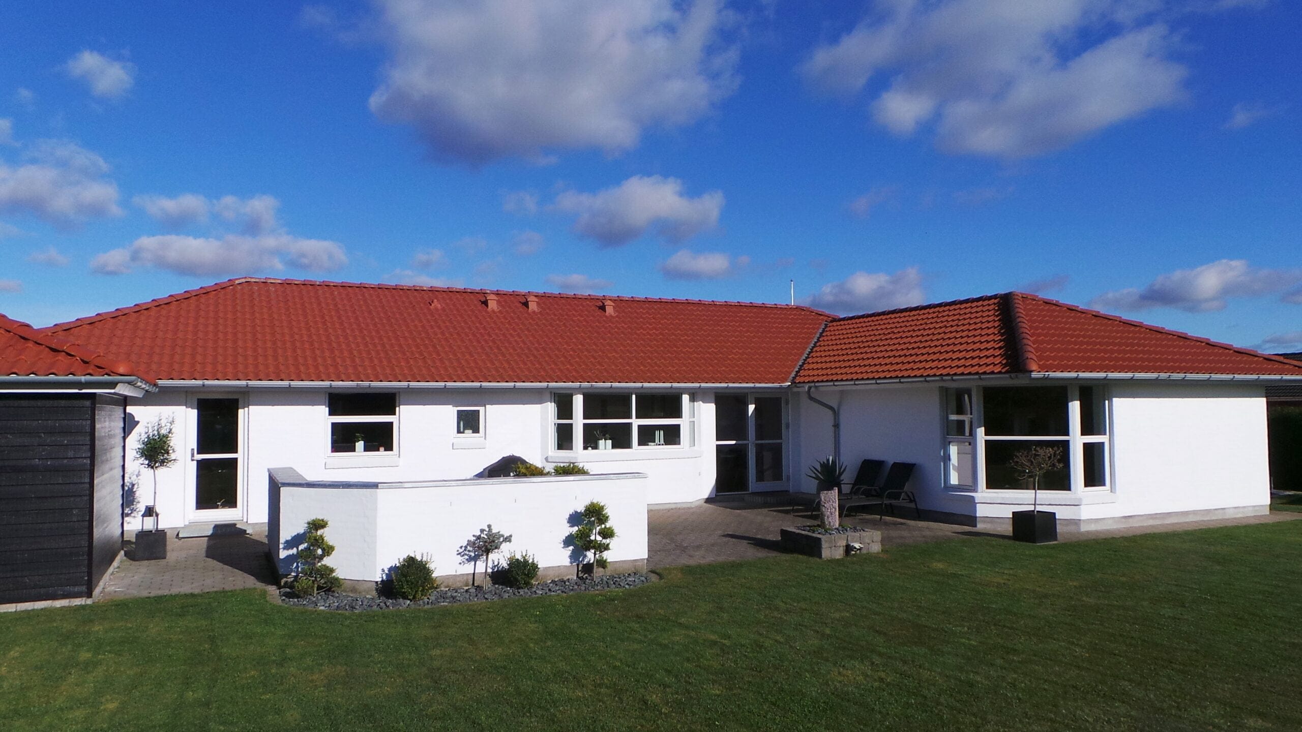 Hvidt hus med rødt tegltag og grøn have