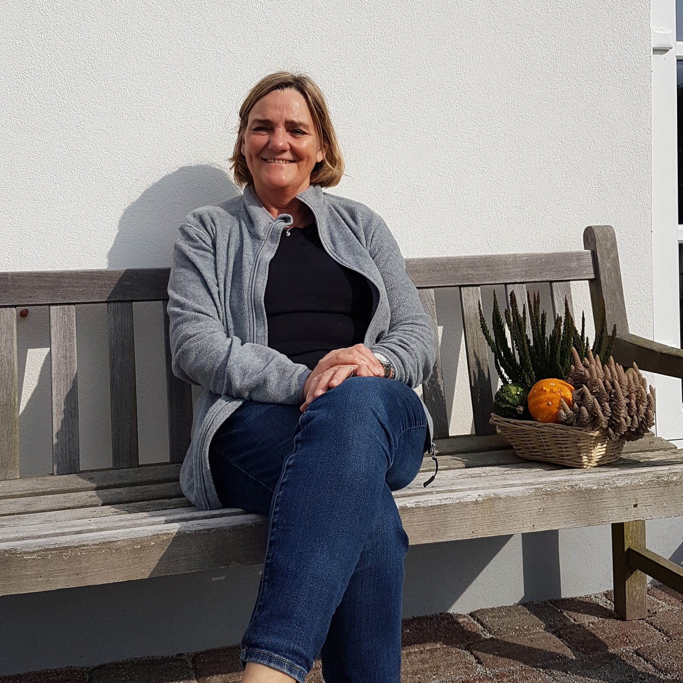 Kvinde sidder på bænk med kurv og planter