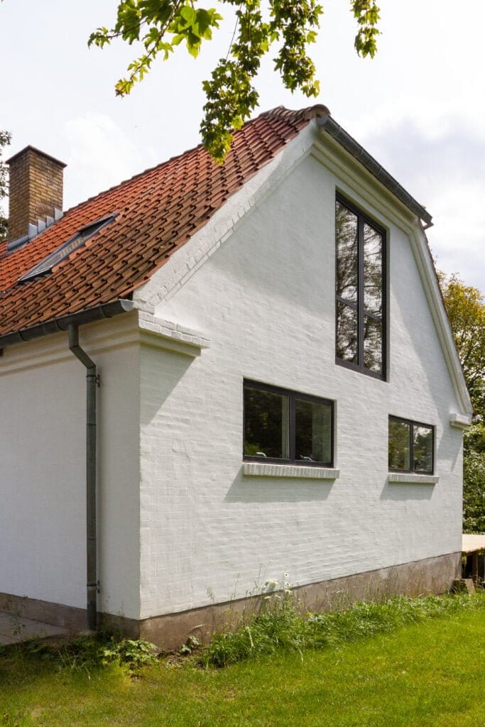 Hvidmuret hus med rødt tegltag og store vinduer